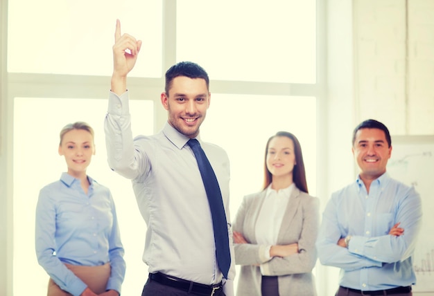 concetto di affari e di ufficio - uomo d'affari bello sorridente con la squadra in ufficio e dito in su