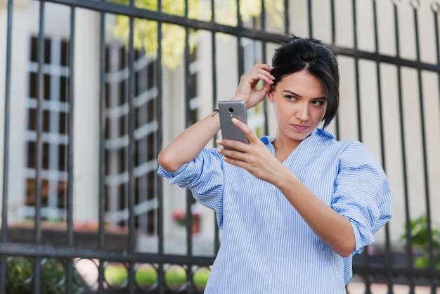 Concetto di affari e stile di vita delle persone Scatto all'aperto di una donna caucasica piuttosto elegante che si sistema i capelli mentre posa per un autoritratto con spazio per la copia del testo