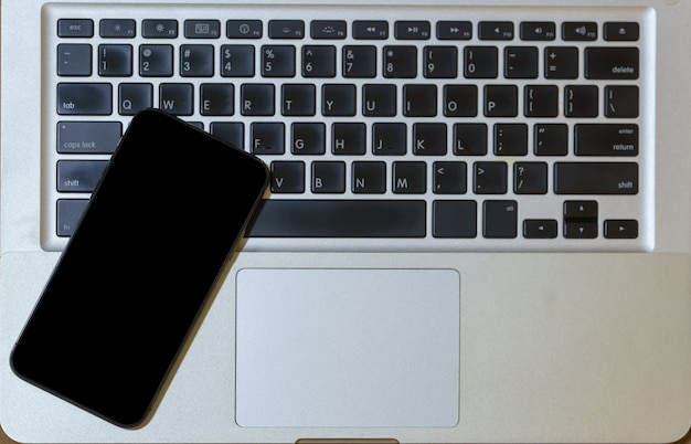 Concetto di affari e tecnologia. Vista dall'alto piatta di uno smartphone mobile con schermo vuoto nero sulla tastiera del computer portatile.