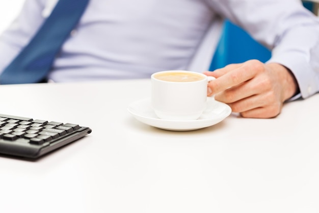 concetto di affari, persone e bevande - primo piano della mano dell'uomo d'affari con la tazza di caffè sul tavolo dell'ufficio