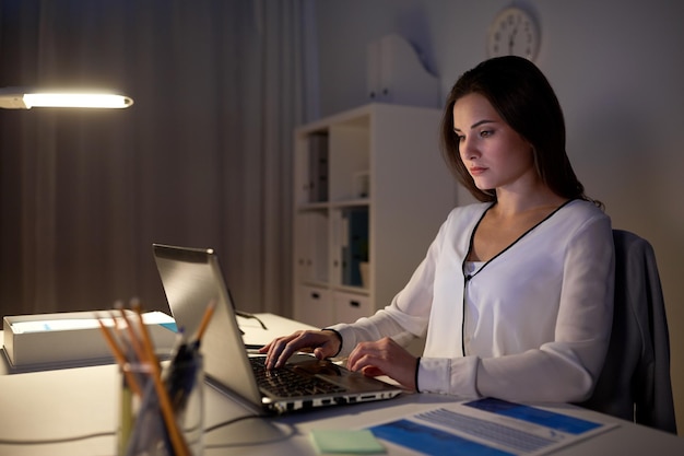 concetto di affari, persone, scadenza e tecnologia - donna d'affari con computer portatile in ufficio notturno