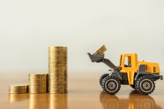 Concetto di affari, soldi, finanza e risparmio. Primo piano di mini camion caricatore in miniatura contengono 4 monete e mettere in cima alla pila di monete d'oro sul tavolo di legno con spazio di copia.