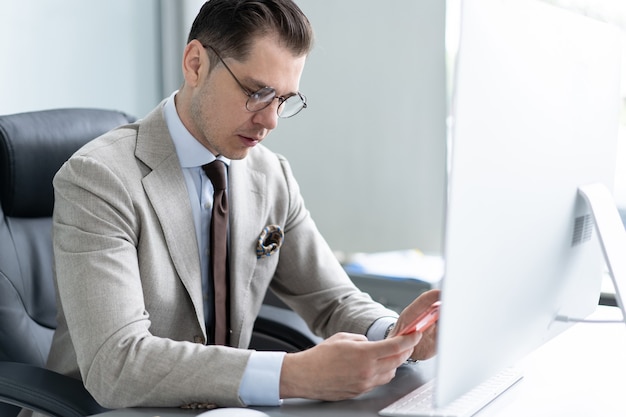 Concetto di affari, ufficio e tecnologia - uomo d'affari con computer e smartphone in ufficio.