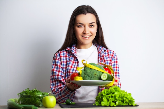 Concetto di alimentazione sana e dieta, verdure della tenuta della ragazza sulla parete di bianco del fondo