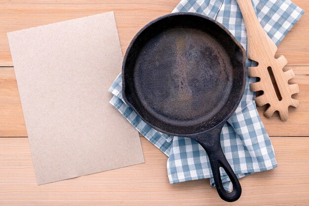 Concetto di alimenti italiani e progettazione del menu padella vuota in ghisa e cucchiaio per la pasta su sfondo di legno