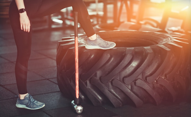 Concetto di allenamento funzionale. Tempo per una pausa. Foto ritagliata di gambe femminili, grande ruota, martello in palestra.