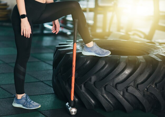 Concetto di allenamento funzionale. Tempo per una pausa. Foto ritagliata di gambe femminili, grande ruota, martello in palestra.