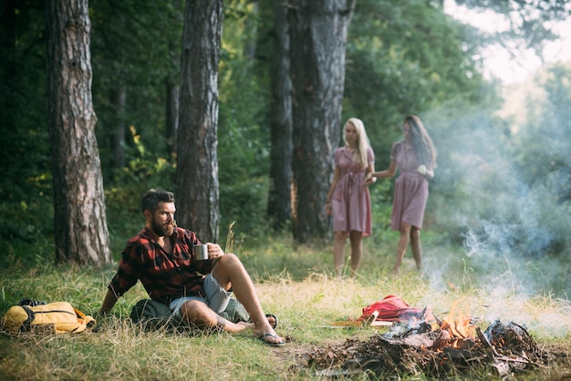 Concetto di ambiente Uomo premuroso che guarda le fiamme del fuoco Due ragazze a piedi nudi che esplorano la foresta