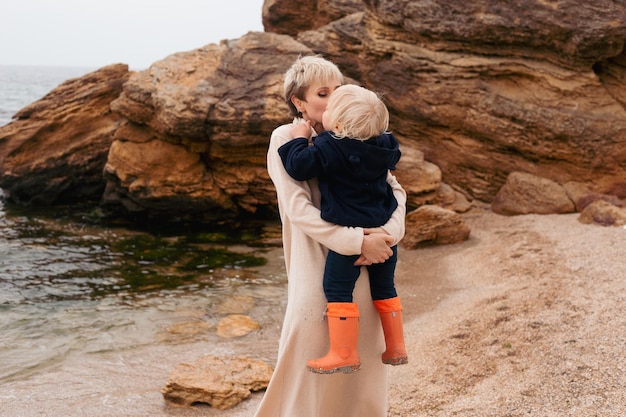 Concetto di amici di famiglia felici per sempre Madre sorridente e figlio piccolo che giocano con la barca di carta insieme vicino al mare in autunno