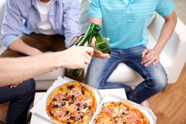 concetto di amicizia, alcol, persone, celebrazione e festività - primo piano di mani maschili che tintinnano bottiglie di birra e mangiano pizza a casa