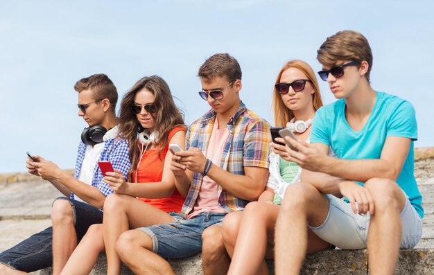 concetto di amicizia, estate, tecnologia e persone - gruppo di amici con smartphone e cuffie all'aperto
