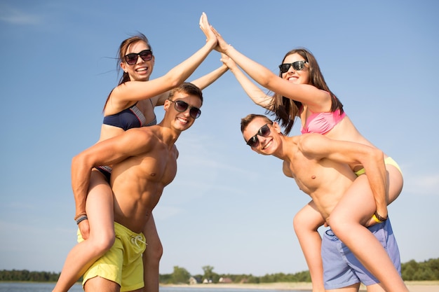 concetto di amicizia, mare, gesto, vacanze e persone - gruppo di amici sorridenti che indossano costumi da bagno divertendosi e facendo il cinque sulla spiaggia