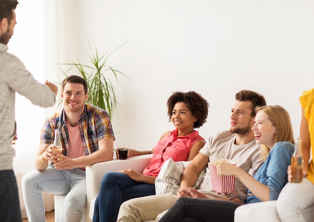 concetto di amicizia, svago, comunicazione e intrattenimento - amici felici con popcorn e bevande che parlano a casa