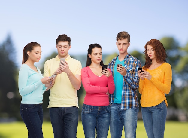 concetto di amicizia, tecnologia e persone - gruppo di adolescenti seri con smartphone sullo sfondo del parco