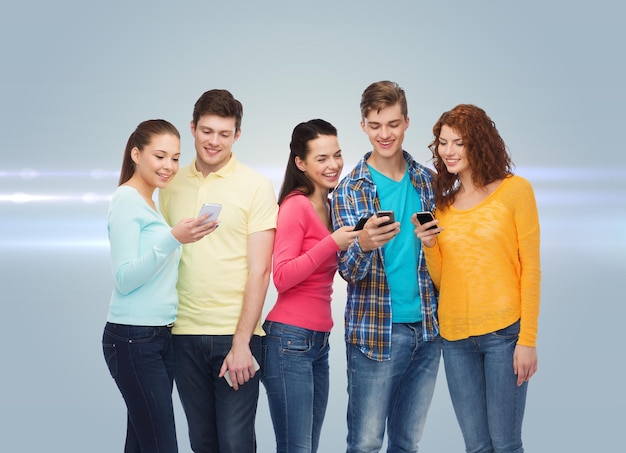 concetto di amicizia, tecnologia e persone - gruppo di adolescenti sorridenti con smartphone su sfondo grigio con luce laser