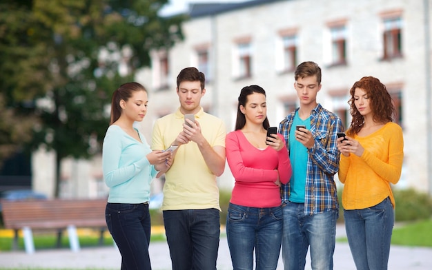 concetto di amicizia, tecnologia, istruzione, scuola e persone - gruppo di adolescenti seri con smartphone sullo sfondo del campus