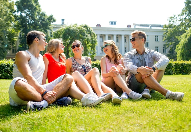 concetto di amicizia, tempo libero, estate e persone - gruppo di amici sorridenti all'aperto seduti e parlando sull'erba sull'erba nel parco