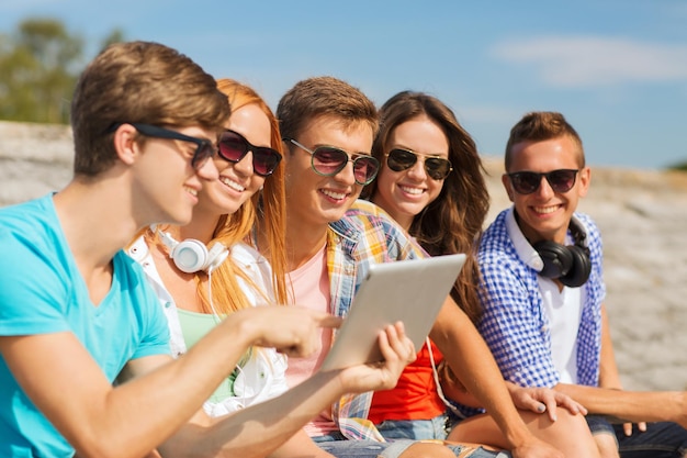 concetto di amicizia, tempo libero, estate e persone - gruppo di amici sorridenti con computer tablet pc seduti all'aperto