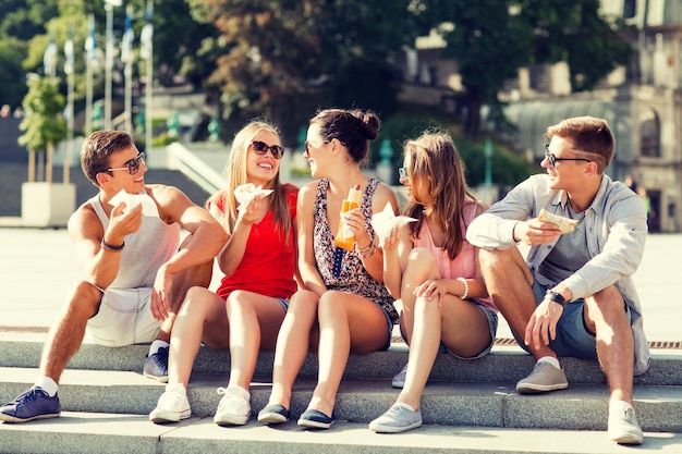 concetto di amicizia, tempo libero, estate e persone - gruppo di amici sorridenti in occhiali da sole seduti con cibo sulla piazza della città