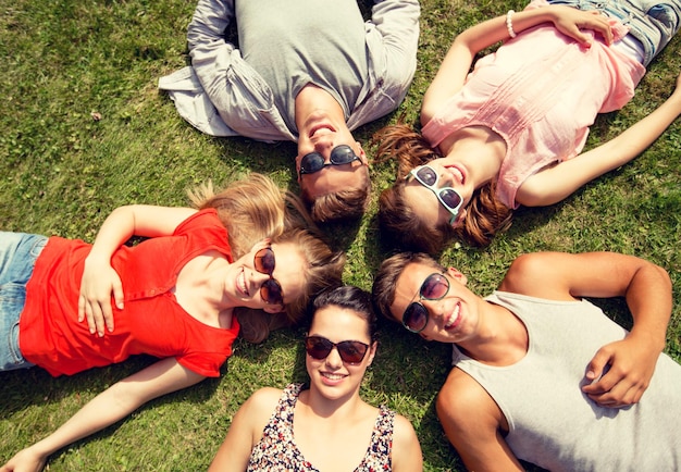 concetto di amicizia, tempo libero, estate e persone - gruppo di amici sorridenti sdraiati sull'erba in cerchio all'aperto