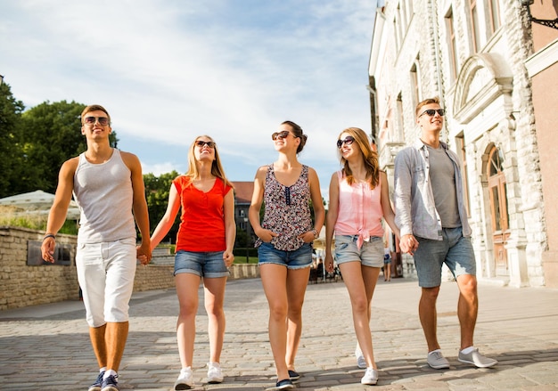 concetto di amicizia, tempo libero, estate, gesto e persone - gruppo di amici sorridenti che camminano e si tengono per mano in città