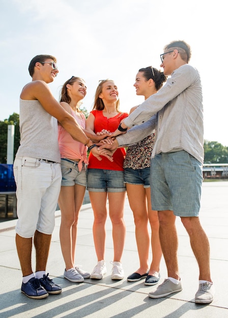 concetto di amicizia, tempo libero, estate, gesto e persone - gruppo di amici sorridenti con le mani in cima in città