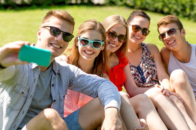 concetto di amicizia, tempo libero, estate, tecnologia e persone - gruppo di amici sorridenti con smartphone che fanno selfie nel parco