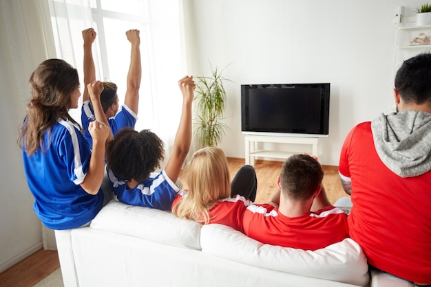 concetto di amicizia, tempo libero, sport, persone e intrattenimento: amici felici o appassionati di calcio che guardano il calcio in tv e celebrano la vittoria a casa