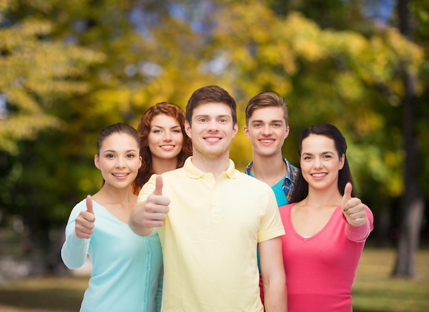 concetto di amicizia, vacanze estive, natura e persone - gruppo di adolescenti sorridenti che mostrano i pollici in su su sfondo verde parco