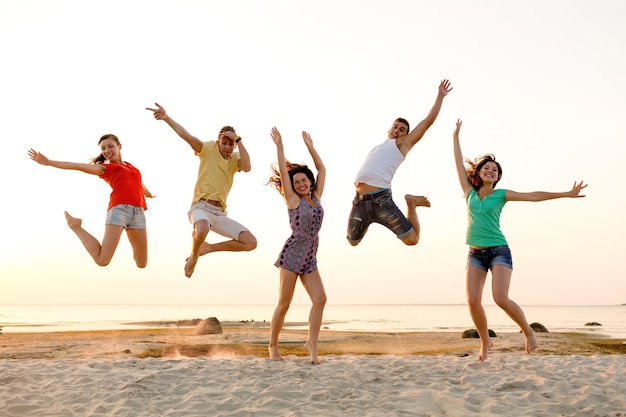 concetto di amicizia, vacanze estive, vacanze, feste e persone - gruppo di amici sorridenti che ballano e saltano sulla spiaggia