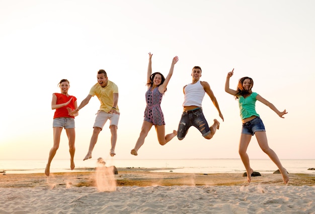 concetto di amicizia, vacanze estive, vacanze, feste e persone - gruppo di amici sorridenti che ballano e saltano sulla spiaggia