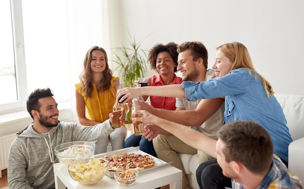 concetto di amicizia, vacanze, fast food e celebrazione: amici felici che fanno festa e tintinnano drink a casa