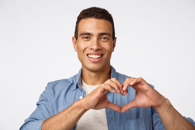 Concetto di amore, amore e affetto. Giovane uomo maschile brasiliano affascinante che mostra il segno e sorridere del cuore felici