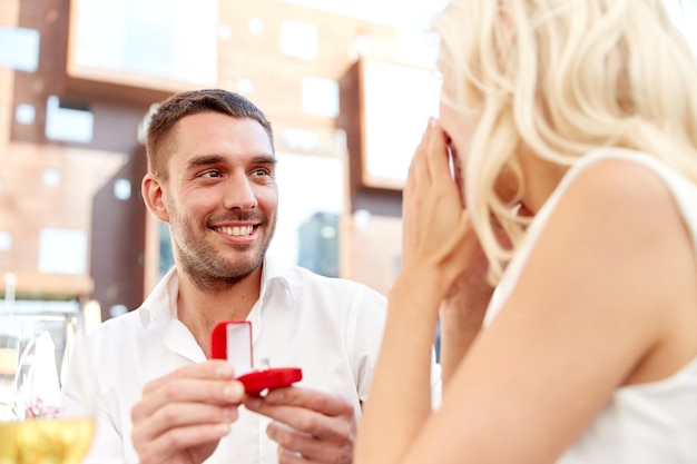 concetto di amore, anniversario, sorpresa, persone e vacanze - uomo felice con anello di fidanzamento che fa proposta alla donna al ristorante