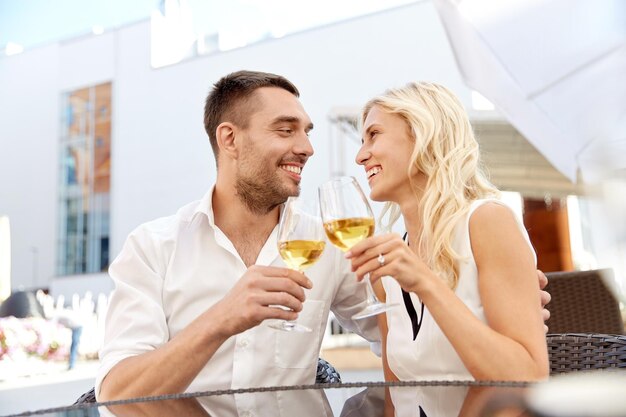 concetto di amore, appuntamenti, persone e vacanze - coppia felice che beve vino al ristorante all'aperto e bicchieri tintinnanti