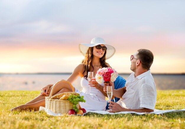 concetto di amore, appuntamenti, persone e vacanze - coppia sorridente che beve champagne durante un picnic su sfondo serale sul mare