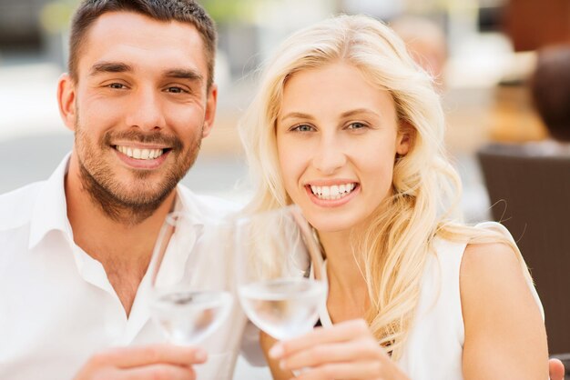 concetto di amore, appuntamenti, persone e vacanze - coppia sorridente che tintinna gli occhiali e si guarda l'un l'altro nella lounge del ristorante o sulla terrazza