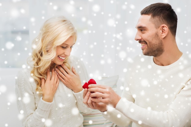 concetto di amore, coppia, relazione, proposta e vacanze - uomo felice che dà un anello di fidanzamento in una piccola confezione regalo rossa alla donna a casa