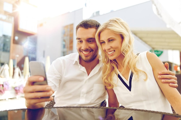 concetto di amore, data, tecnologia, persone e relazioni - coppia felice sorridente che prende selfie con lo smatphone sulla terrazza del ristorante