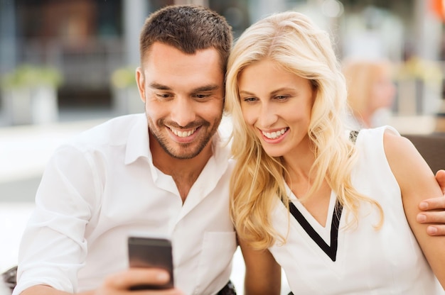 concetto di amore, data, tecnologia, persone e relazioni - coppia felice sorridente con smatphone al caffè della strada della città