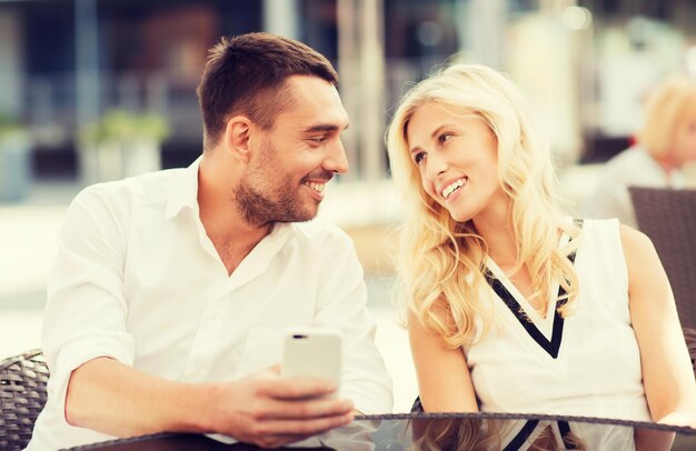 concetto di amore, data, tecnologia, persone e relazioni - coppia felice sorridente con smatphone al caffè della strada della città