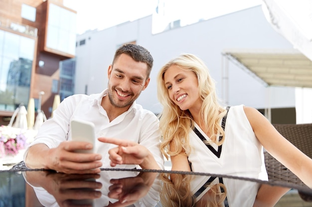 concetto di amore, data, tecnologia, persone e relazioni - coppia felice sorridente con smatphone sulla terrazza del ristorante