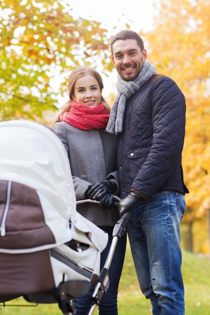 concetto di amore, genitorialità, famiglia, stagione e persone - coppia sorridente con carrozzina nel parco autunnale