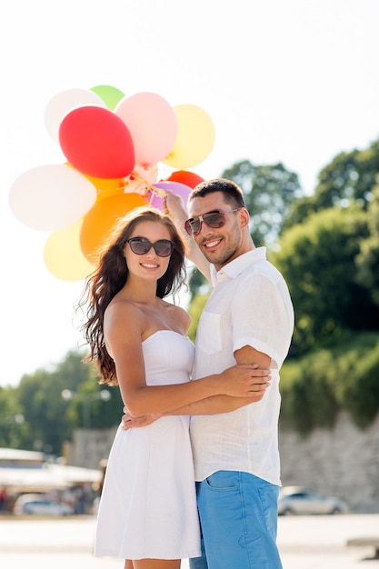 concetto di amore, matrimonio, estate, appuntamenti e persone - coppia sorridente che indossa occhiali da sole con palloncini che si abbracciano nel parco