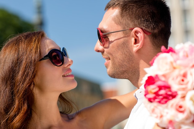concetto di amore, matrimonio, estate, appuntamenti e persone - coppia sorridente che indossa occhiali da sole con un mazzo di fiori che si abbracciano in città