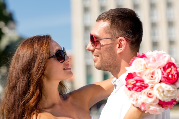 concetto di amore, matrimonio, estate, appuntamenti e persone - coppia sorridente che indossa occhiali da sole con un mazzo di fiori che si abbracciano in città