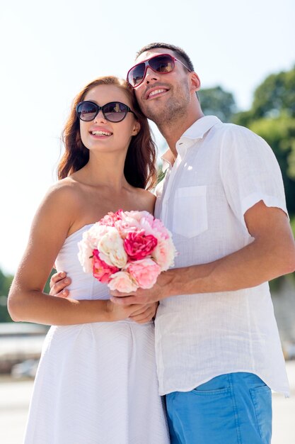 concetto di amore, matrimonio, estate, appuntamenti e persone - coppia sorridente che indossa occhiali da sole con un mazzo di fiori che si abbracciano in città