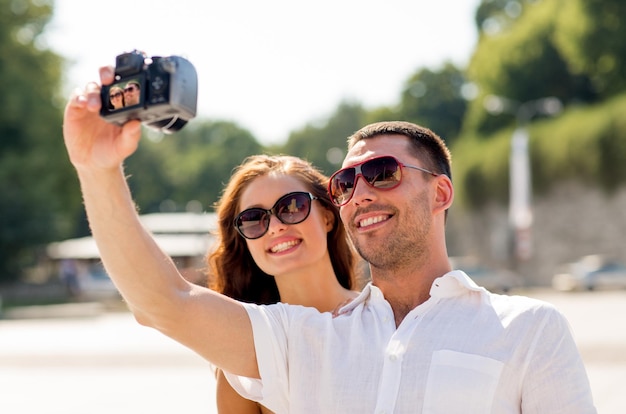 concetto di amore, matrimonio, estate, appuntamenti e persone - coppia sorridente che indossa occhiali da sole facendo selfie con la fotocamera digitale nel parco