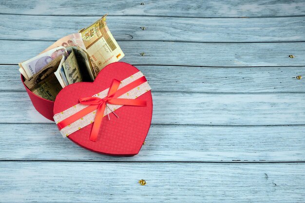 Concetto di amore per il denaro, in una scatola che è un cuore sopra un tavolo di legno blu.
