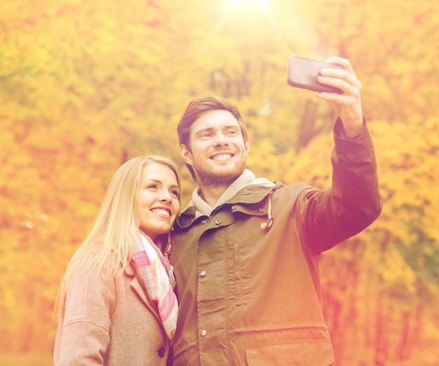 concetto di amore, relazione, famiglia e persone - coppia sorridente che si abbraccia e si fa selfie nel parco autunnale